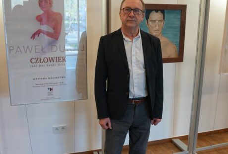 fotografia przedstawia mężczyznę, artystę malarza na tle nowej wystawy w MDK Ratusz.