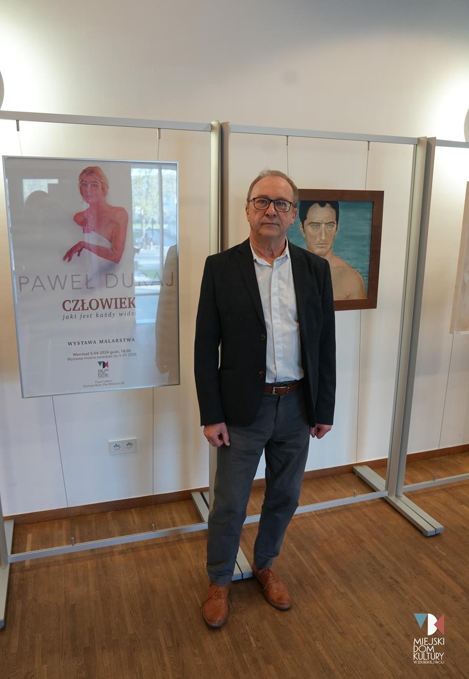 fotografia przedstawia mężczyznę, artystę malarza na tle nowej wystawy w MDK Ratusz.