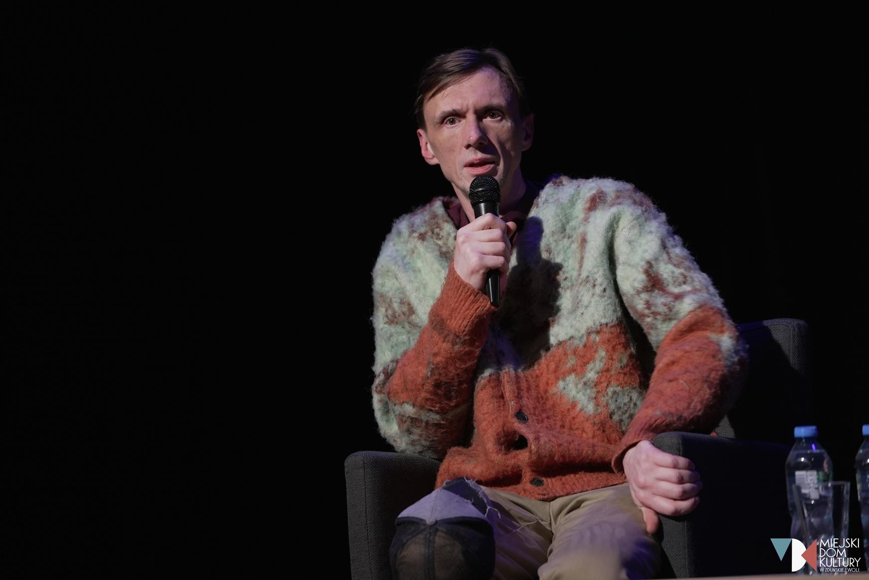 zdjęcie przedstawia młodego aktora, mężczyznę w krótkich włosach z mikrofonem w dłoni, to Andrzej Kłak, z którym spotkanie odbyło się 16 grudnia.