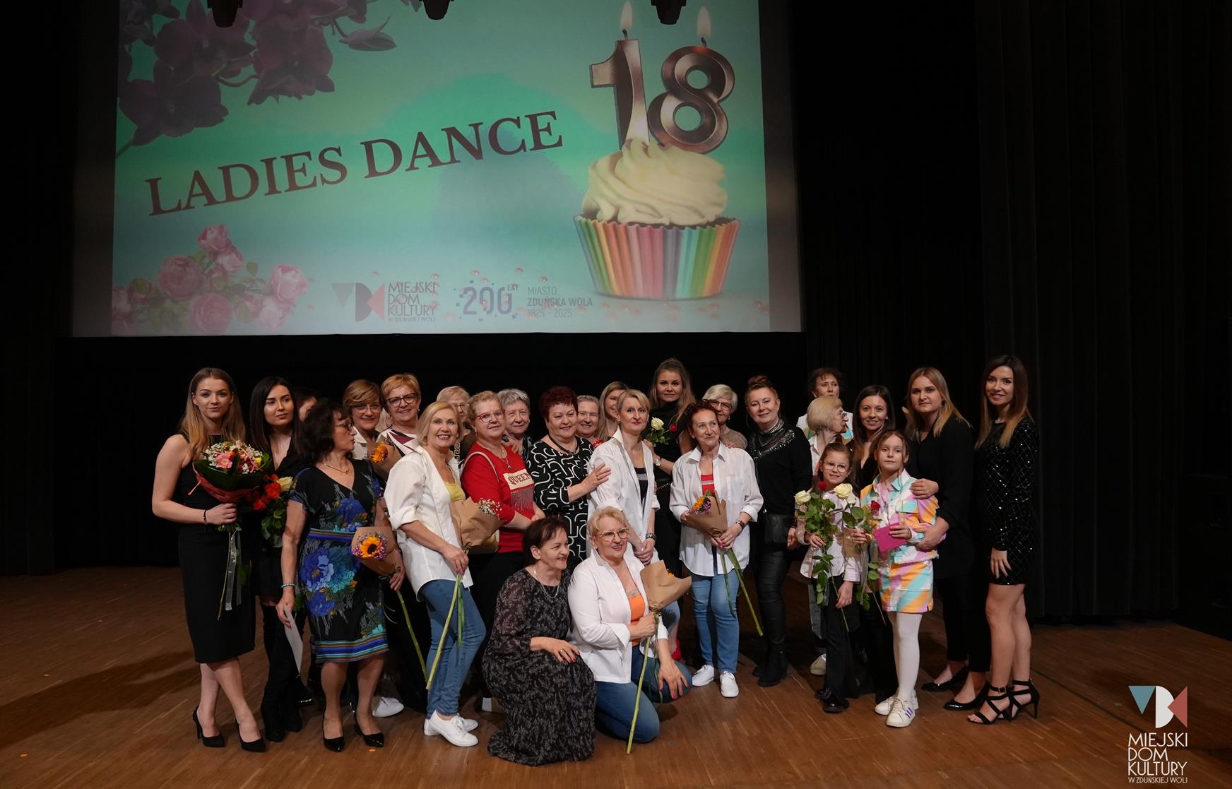 zdjęcie przedstawia ok 40 osób na scenie w Ratuszu, to tancerki Ladies Dance i członkinie zespołu wokalnego Rezonans podczas koncertu osiemnastka Ladies Dance