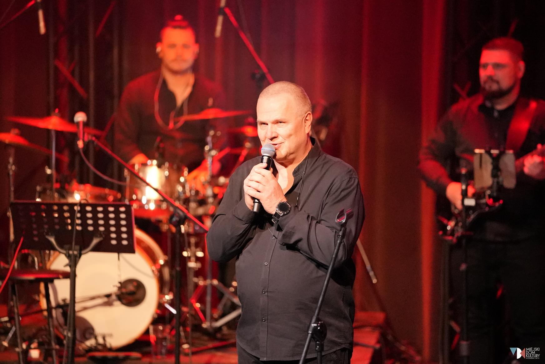 Zdjęcie przedstawia gospodarza wieczoru Andrzeja Wawrzyniaka, mężczyzna w średnim wieku, z mikrofonem w dłoni, na scenie w Ratuszu