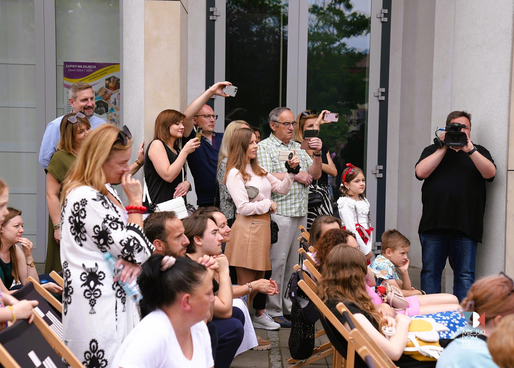 zdjęcie przedstawia kilkanaście osób, które siedzą i stoją i patrzą na występy swoich dzieci