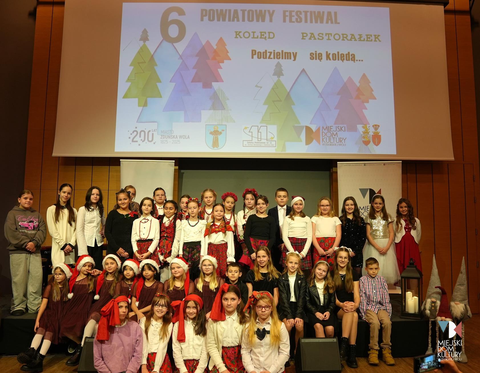 zdjęcie przedstawia kilkadziesiąt osób na scenie , to uczestnicy Festiwalu Kolęd i Pastorałek, dzieci ubrane w świąteczne stroje