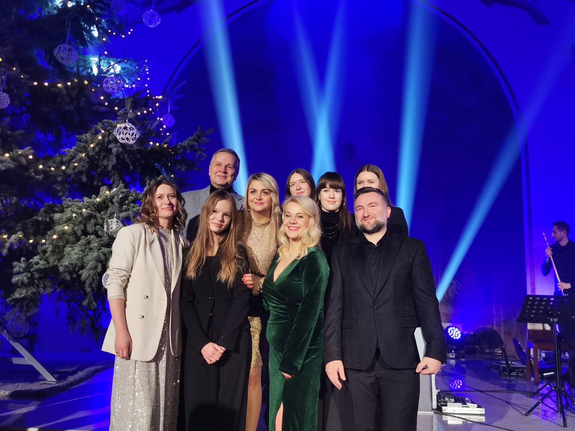 zdjęcie przedstawia wokalistki z Klubu Piosenki A' priori, jurorów i Andrzeja Wawrzyniaka, laureatów I nagrody w kategorii zespoły wokalne festiwalu w Pajęcznie, grupa uśmiechniętych osób stoi na tle choinki