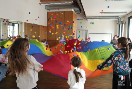 zdjęcie przedstawia dzieci, kilkanaście os&oacute;b przy kolorowej chuście animacyjnej