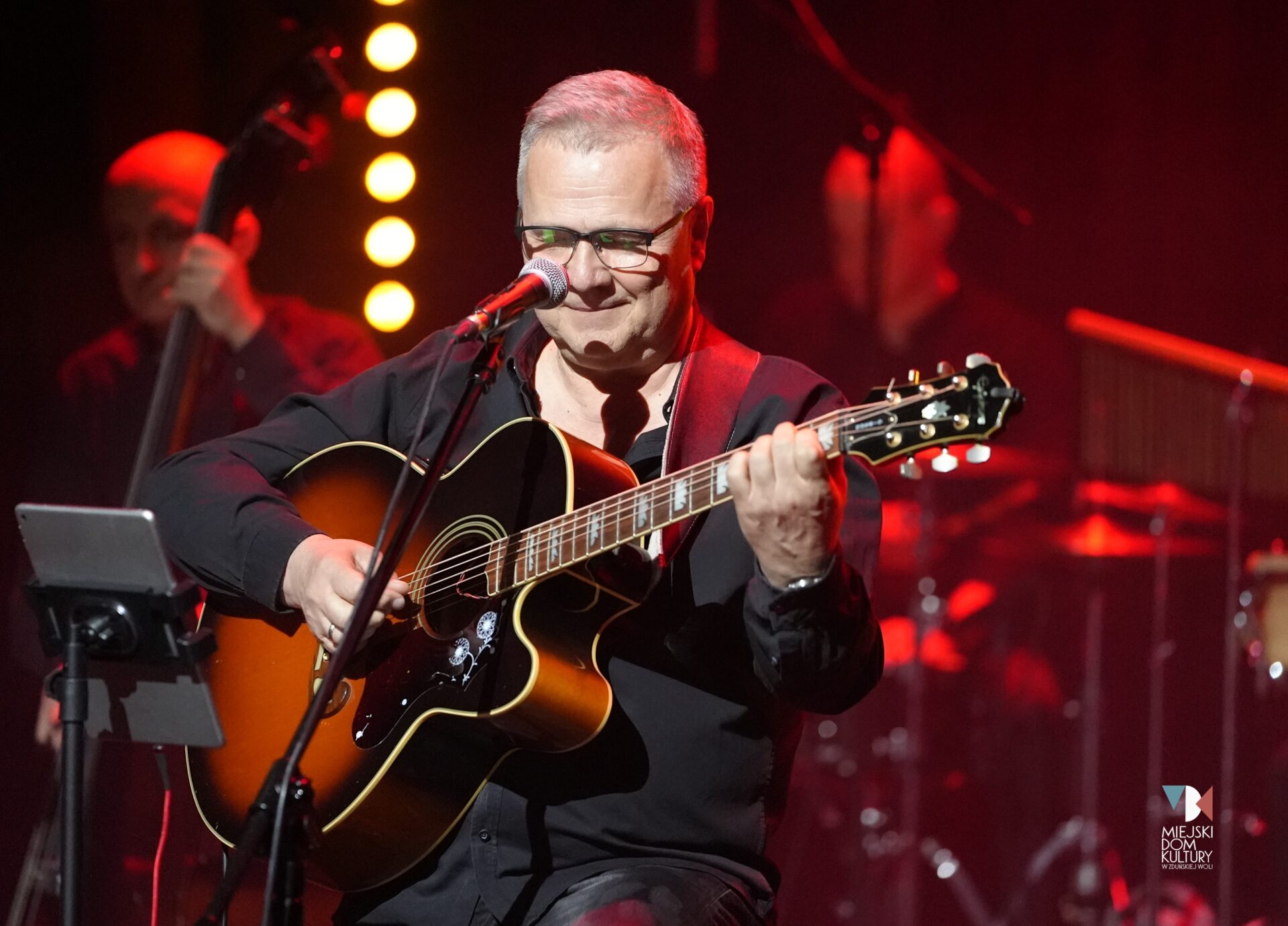 zdjęcie przedstawia Andrzeja Wawrzyniaka z gitarą ręku, starszy mężczyzna, muzyk na scenie