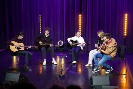 zdjęcie przedstawia pięć os&oacute;b na z gitarami, kt&oacute;re siedzą na czarnych krzesłach