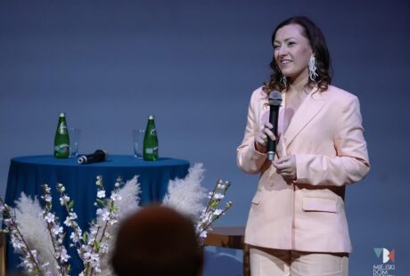 zdjęcie przedstawia kobietę w średnim wieku z uśmiechem na ustach w jasnym garniturze i w ciemnych długich włosach