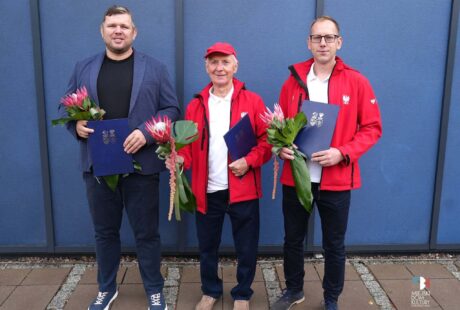Zdjęcie przedstawia trzech sportowców Dominika Szewczyka, Zenona Kowalczyka i Tomasza Słowiksowskiego, na tle niebieskiej ściany