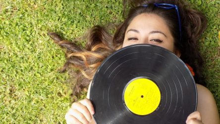 zdjęcie przedstawia młodą dziewczynę z płytą winylową w ręku na zielonej trawie