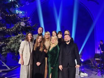 zdjęcie przedstawia wokalistki z Klubu Piosenki A' priori, jurorów i Andrzeja Wawrzyniaka, laureatów I nagrody w kategorii zespoły wokalne festiwalu w Pajęcznie, grupa uśmiechniętych osób stoi na tle choinki