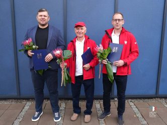 Zdjęcie przedstawia trzech sportowców Dominika Szewczyka, Zenona Kowalczyka i Tomasza Słowiksowskiego, na tle niebieskiej ściany