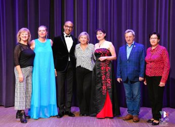 zdjęcie przedstawia siedem osób, to śpiewacy operowi i zarząd uniwersytetu trzeciego wieku na scenie w sali widowiskowej Ratusz podczas koncertu muzyki filmowej