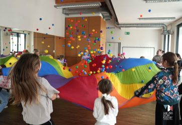 zdjęcie przedstawia dzieci, kilkanaście osób przy kolorowej chuście animacyjnej