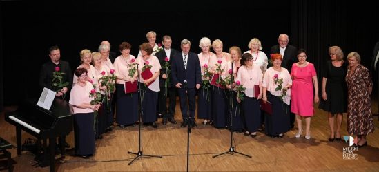 zdjęcie przedstawia 21 osób kobiety i mężczyzn z sekcji wokalnej UTW i zarząd UTW na scenie w Ratuszu