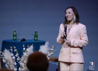 zdjęcie przedstawia kobietę w średnim wieku z uśmiechem na ustach w jasnym garniturze i w ciemnych długich włosach